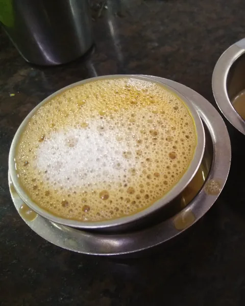 Frothy South Indian filter coffee in a steel tumbler and dabarah.